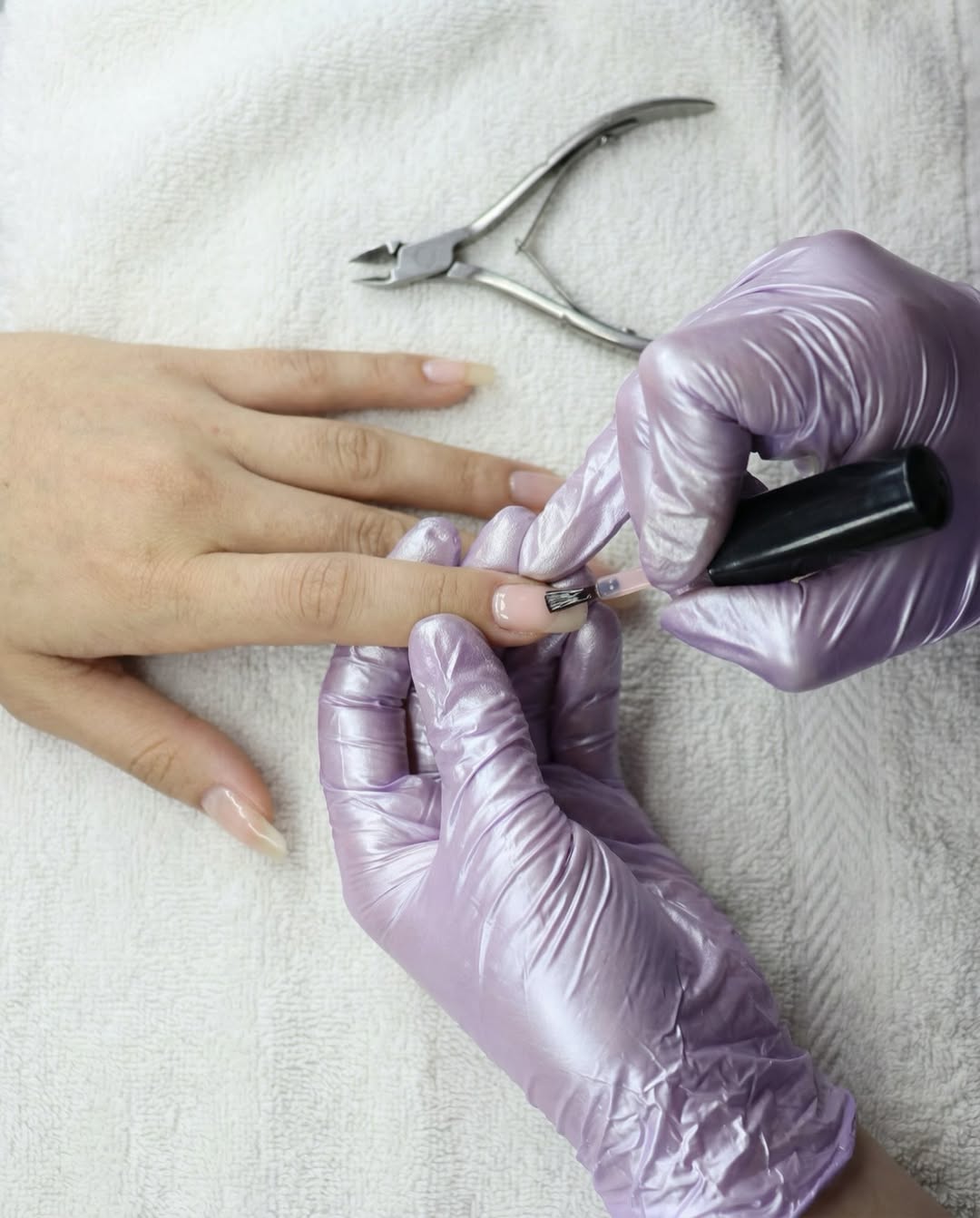 Manicurista con guantes lavanda aplicando gel en Alma Mía